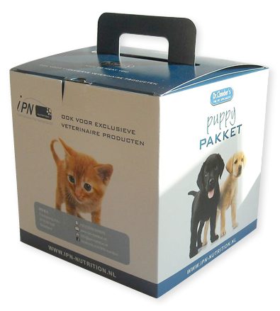 Een vierkante, op maat gemaakte kartonnen doos met handvat van 17x17x17 cm, uitgevoerd als een 'Puppy Pakket' welkomstpakket. De verpakking is volledig bedrukt in full color met een zakelijke en frisse uitstraling: de bovenzijde is donkerblauw met een geïntegreerd zwart handvat, terwijl de witte zijvlakken zijn voorzien van vertederende foto's van een rode kitten en twee puppy's (een zwarte en een blonde Labrador). De tekst 'puppy PAKKET' en 'OOK VOOR EXCLUSIEVE VETERINAIRE PRODUCTEN' is duidelijk leesbaar, samen met het logo van 'ipn nutrition' en contactgegevens onderaan. Deze doos is een perfect voorbeeld van hoe een verpakking met handvat wordt gebruikt als bedrukte goodiebag of welkomstpakket bij een event, waarbij het stevige vouwkarton zorgt voor een premium uitstraling en goed draagvermogen voor veterinaire producten.