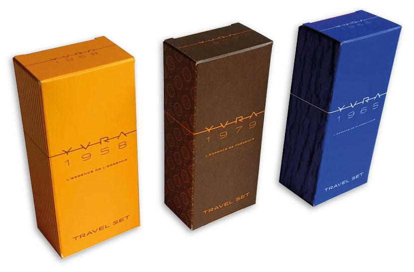 Een close-up van drie identieke, hoge, rechthoekige parfumdoosjes op maat voor de Yvra travel set parfum, die de consistentie in vorm maar variatie in kleur benadrukken voor verschillende geuren. Drie Kleuren, Drie Geuren: De doosjes zijn gekleurd in (van links naar rechts) fel oranje, donker bruin, en fel blauw. Dit illustreert hoe de parfumdoosjes in 3 opdrukken zijn gemaakt om elke geur te onderscheiden. Design en Opdruk: Elk doosje heeft een strak, modern design. De merknaam 