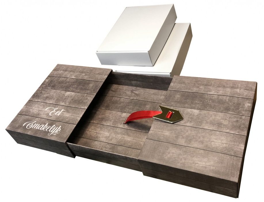 Transformatieve Golfkartonnen Ontbijtbox/Tafeldoos (3 Afbeeldingen) Deze drie afbeeldingen tonen de transformatie en het ingenieuze ontwerp van een originele doos van golfkarton die fungeert als een ontbijtbox en kan worden uitgeklapt tot een kleine tafel. Vormgeving en Constructie (Transformatie): De doos is bedrukt met een realistisch fotoprint van verweerd, grijsbruin hout in een full color opdruk, wat de illusie van een houten tafel creëert. Afbeelding 1 (Gesloten Box/Gedeeltelijk Uitgeklapt): Dit toont de doos als een langwerpige geschenkdoos met een vast compartiment in het midden (in dit geval twee witte binnendozen zijn zichtbaar) en twee uitklapbare zijpanelen die als tafelbladen dienen. Op het linkerzijpaneel staat de pakkende tekst 