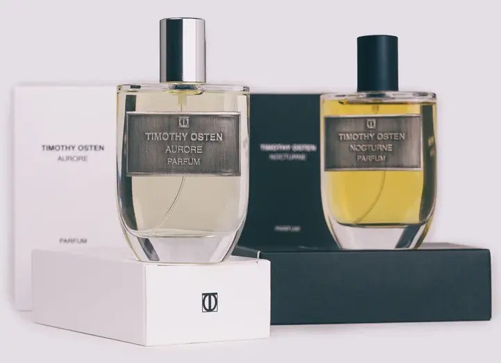 Een opstelling van twee luxe parfumflesjes en twee parfumdoosjes op maat van het merk Timothy Osten, die een minimalistische, elegante en consistente merkbeleving tonen. Parfumflesjes: Er staan twee identieke, rechthoekige glazen parfumflesjes centraal opgesteld. Het flesje links bevat een lichtgele, bijna transparante vloeistof (