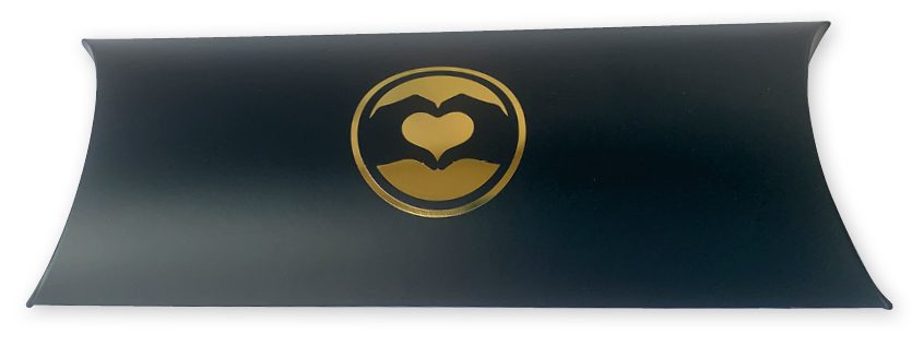 Een exclusief mat zwart bedrukt gondeldoosje (pillow box) van 220 x 110 x 40 mm, voorzien van een luxe logo in goudfolie-bedrukking. Het doosje heeft de kenmerkende elegante ronde vormen van een kussendoosje en toont centraal een goudkleurig symbool van twee handen die een hart vormen. Deze speciale uitvoering illustreert hoe een gondeldoosje met logo als hoogwaardige cadeauverpakking of productverpakking direct de aandacht trekt. Dankzij de luxe afwerking met goudfolie krijgt de verpakking een unieke en professionele uitstraling, perfect voor een bijzonder geschenk, een luxe cadeaubon of een onderscheidende giftcard