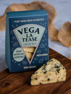 Een luxe bedrukte doos voor plantaardige kaas van het merk Vega La Tease, uitgevoerd in een stijlvolle donkerblauwe kleur met een driehoekig venster dat de