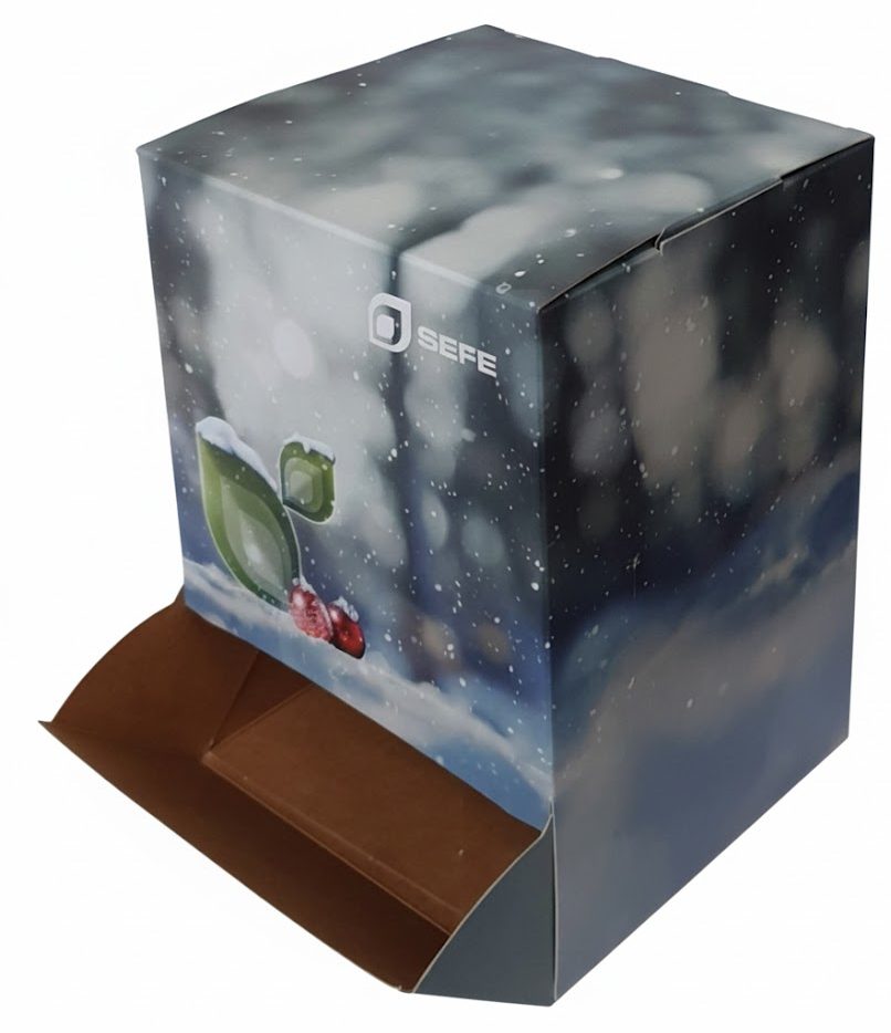 Een close-up, lichte studiofoto toont een kubusvormige kartonnen dispenserdoos met een full color bedrukking in een winters, kerst- of feestdag-thema voor het merk SEFE. De doos is bedrukt met een sfeervolle, wazige achtergrond van donkerblauwe, grijze en witte tinten, wat een sneeuwlandschap of nachtelijke buitenomgeving suggereert. Er zijn witte 'sneeuwvlokken' op de voorgrond gedrukt, waardoor een diepte-effect ontstaat. In het midden van de afbeelding is een detail te zien van een felgroen blad met sneeuw, dat op een bes of rood voorwerp rust in de sneeuw. Bovenaan de doos staat het logo van het merk 