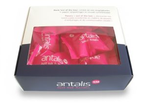 Een professionele, vierkante bedrukte doos met venster voor het bedrijf Antalis, gevuld met roze verpakte gelukscookies. De kartonnen vensterdoos heeft een tweekleurig ontwerp: een witte bovenkant met de tekst "Denk 'out of the box'" in het Nederlands en Frans, en een donkerblauwe onderzijde met het logo "Antalis - Just ask Antalis". Door het grote, rechthoekige transparante venster in het deksel zijn de felroze individueel verpakte koekjes duidelijk zichtbaar. Deze maatwerk verpakking dient als voorbeeld van een vensterdoosje dat productherkenning verhoogt, de klant overtuigt door zichtbaarheid van kleur en vorm, en beschadiging van de verpakking voorkomt.