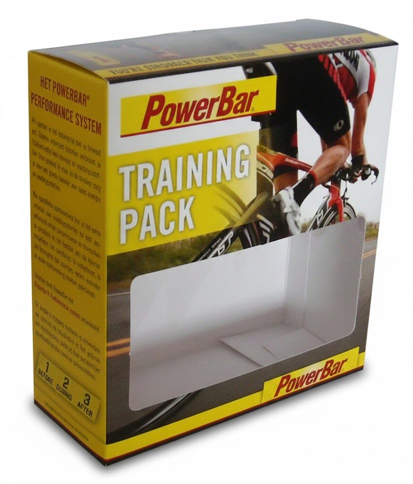 Een op maat gemaakte, bedrukte doos met venster voor een PowerBar Training Pack, uitgevoerd in een sportief ontwerp met de kleuren geel, wit en zwart. De kartonnen vensterdoos toont een actieafbeelding van een wielrenner en bevat gedetailleerde informatie over het 'Performance System' (Before, During, After). Het grote, rechthoekige venster in het midden van de verpakking is strategisch geplaatst om het product aan de klant te laten zien voordat hij het doosje openmaakt. Deze functionele productverpakking geeft de juiste uitstraling aan het merk, stelt de consument in staat de inhoud goed te beoordelen en voorkomt dat de verpakking in de winkel wordt geopend of beschadigd, wat de kans op retouren aanzienlijk vermindert.