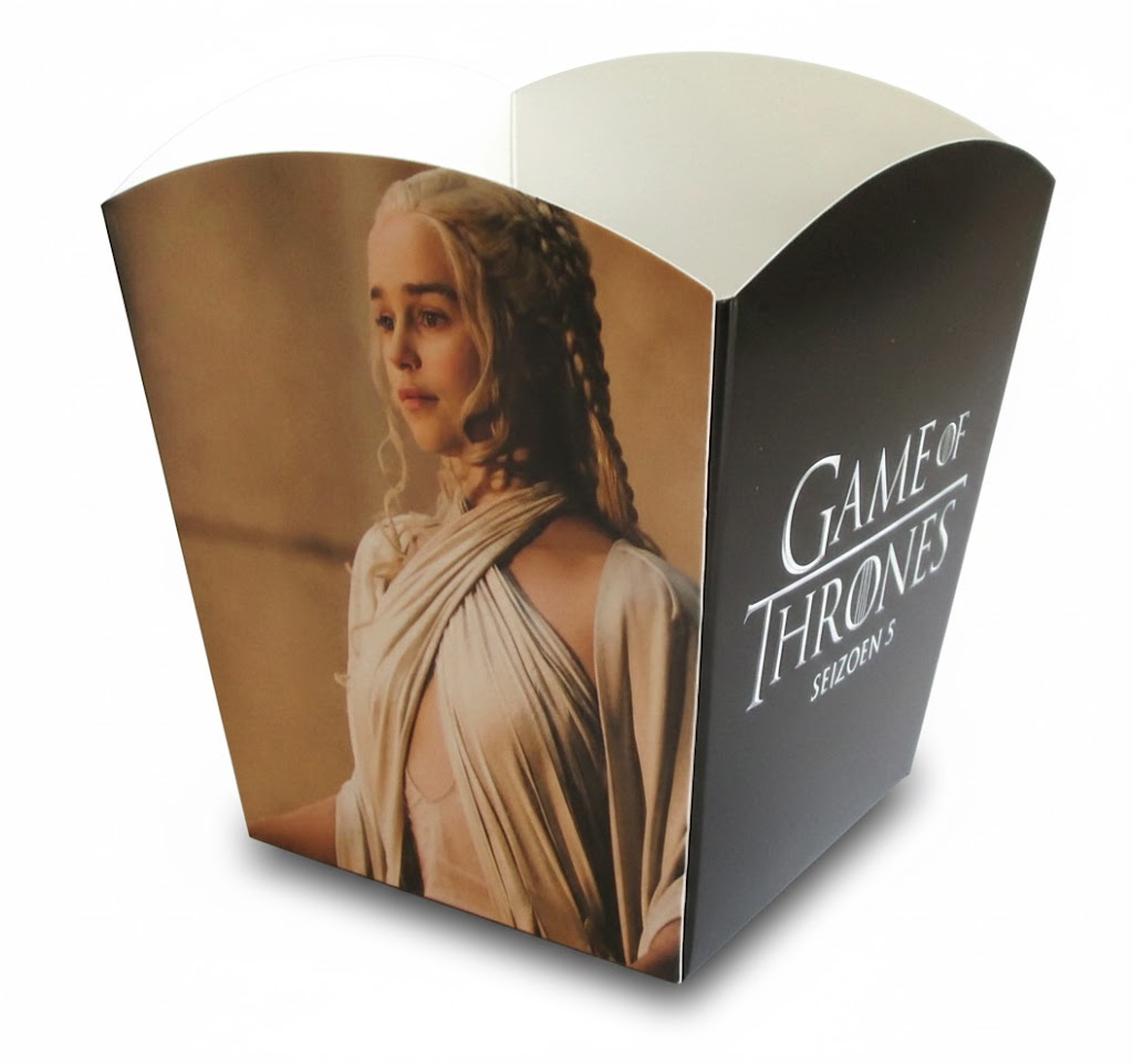Een close-up van een professioneel bedrukt popcornbakje, uitgevoerd als promotieartikel voor de serie 'Game of Thrones Seizoen 5'. Het bakje is vervaardigd uit stevig, licht glanzend en voedselveilig karton en heeft een klassieke geschulpte (gegolfde) bovenrand. De full color bedrukking toont op de linkerzijde een gedetailleerd portret van het personage Daenerys Targaryen in een zandkleurige omgeving. De rechterzijde van het bakje is uitgevoerd in diepzwart met daarop in strakke, witte letters het officiële logo 'GAME OF THRONES' en de tekst 'SEIZOEN 5'. Dit bakje is een praktijkvoorbeeld van hoe een gepersonaliseerde popcornverpakking met autolock bodem wordt ingezet bij een filmpremière of serie-lancering om een merk direct in de schijnwerpers te zetten met een professionele uitstraling.