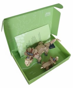 De geopende binnenzijde van een op maat gemaakte groene speelgoeddoos voor een Lego bouwpakket van een Triceratops met jong. De binnenzijde is volledig full-color bedrukt met witte lijntekeningen van bladeren en een stippellijn met de tekst "Knip uit om mee te spelen". In de doos ligt een bedrukte bijsluiter bij de dino-figuren. Dit toont aan hoe zowel de binnen- als buitenkant van een doos benut kan worden voor een complete en aantrekkelijke productervaring.