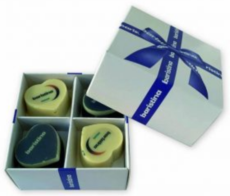 Close-up van een kleine, witte, vierkante giftset of cadeaudoos met los deksel die perfect is als doosje voor kaarten of bonbons. Het deksel, dat is versierd met een glanzend blauw satijnen lint en strik, is van de onderdoos geschoven en staat rechtsboven, schuin geplaatst ten opzichte van de onderdoos. Het blauwe lint is bedrukt met het woord