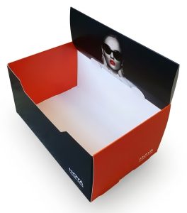 Een schuine bovenaanzicht-opname van een open kartonnen verpakkings- of presentatiedoos op een effen witte achtergrond. De doos heeft een strakke, eigentijdse vormgeving. De buitenkant is matzwart aan de voorkant en zijkanten, terwijl de binnenkant een levendige oranje-rode tint heeft. Een deel van de zwarte voorflap is naar boven geklapt, wat een close-up toont van het gezicht van een vrouw met donkere zonnebril en rode lippenstift. De binnenkant van de doos is grotendeels leeg en laat een witte bodem zien, geschikt voor het plaatsen van producten. De hoeken zijn scherp en de afwerking ziet er hoogwaardig uit. De verlichting is gelijkmatig en helder, wat de kleuren en details van de verpakking accentueert.