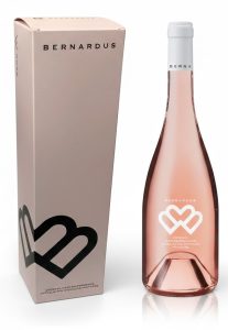 Luxe wijnverpakking op maat in een zachtroze uitvoering voor Bernardus Rosé, met een bijpassende slanke wijnfles rechts naast de doos. De fles is exact even hoog als de kartonnen koker, wat de perfecte pasvorm van dit maatwerk benadrukt. Deze gepersonaliseerde flessendoos is geproduceerd in onze eigen drukkerij in Berkel en Rodenrijs met Cradle to Cradle gecertificeerde inkt en 100% groene stroom. Een hoogwaardige verpakking die vakmanschap uitstraalt, beschikbaar voor afnames vanaf 50 stuks.
