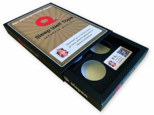Een bovenaanzicht van een luxe, dubbelwandige bedrukte sleeve die functioneert als schuifdoos voor Sleep Well Tape. De buitenste sleeve is uitgevoerd in een matzwarte afwerking met goudkleurige en witte belettering, wat een hoogwaardige uitstraling geeft. De binnenzijde van de schuifverpakking bevat een zwart kartonnen interieur met twee ronde uitsparingen voor de tape-rollen en een bedrukte kortingskaart met QR-code. De bovenzijde van de sleeve toont een centraal 'Sleep Well Tape' logo op een bruine achtergrond met een straalpatroon. Het ontwerp is voorzien van functionele teksten en instructies, en de zijkanten zijn bedrukt met de slogan 'heerlijk slapen'. Dit is een uitstekend voorbeeld van een op maat gemaakte, stevige kartonnen schuifhuls die zowel bescherming als een luxe uitpakervaring (unboxing) biedt voor e-commerce en retail.