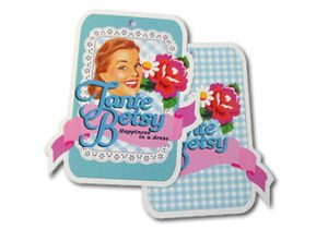 Twee kleurrijke hangtags voor het kledingmerk Tante Betsy, uitgevoerd in een unieke contourvorm met afgeronde hoeken en uitgestanste details. De voorste tag toont een retro-illustratie van een lachende vrouw met rode rozen tegen een blauw-wit geruit (gingham) patroon. Een roze wimpel met de tekst 'Happiness in a dress' krult over het ontwerp heen. De achterste tag toont de binnenzijde met hetzelfde ruitjespatroon. Bovenaan bevindt zich een klein, gecentreerd boorgat. De kleuren zijn helder en verzadigd, wat wijst op hoogwaardig full color drukwerk op wit karton.