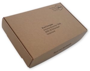 Een rechthoekige brievenbusdoos van natuurlijk bruin kraft karton met een matte textuur, schuin van boven gefotografeerd tegen een witte achtergrond. De bovenkant is gepersonaliseerd met een strakke zwarte bedrukking: rechtsboven het 'Port Betaald' logo van PostNL en in het midden de bedrijfsnaam BrainCompass met adresgegevens in Rotterdam. Op de voorste zijrand van de doos staat in een modern lettertype de tekst 'Seal on backside' gedrukt. De verpakking is op maat geproduceerd door Drukkerij Van der Louw.