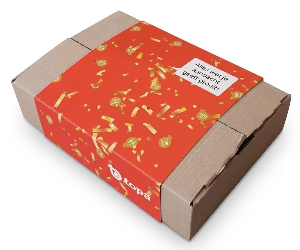 Een schuin bovenaanzicht van een vrijstaand, bruin kartonnen verzenddoosje, veredeld met een op maat gemaakte kartonnen sleeve. De verpakkingswikkel is felrood bedrukt met een vrolijk patroon van strooi-goldconfetti en kleine, circular '100 jaar' emblemen. Rechtsboven op de sleeve is een tekstwolkje uitgespaard met de duidelijke Nederlandse tekst: 'Alles wat je aandacht geeft groeit!'. Op de zijkant is subtiel het logo 'topa' verwerkt. Deze bedrukte sleeve toont hoe een standaard e-commerce verpakking met een lage investering getransformeerd wordt tot een premium, feestelijke unboxing ervaring voor retail en zakelijke geschenken. Geproduceerd in Berkel en Rodenrijs.