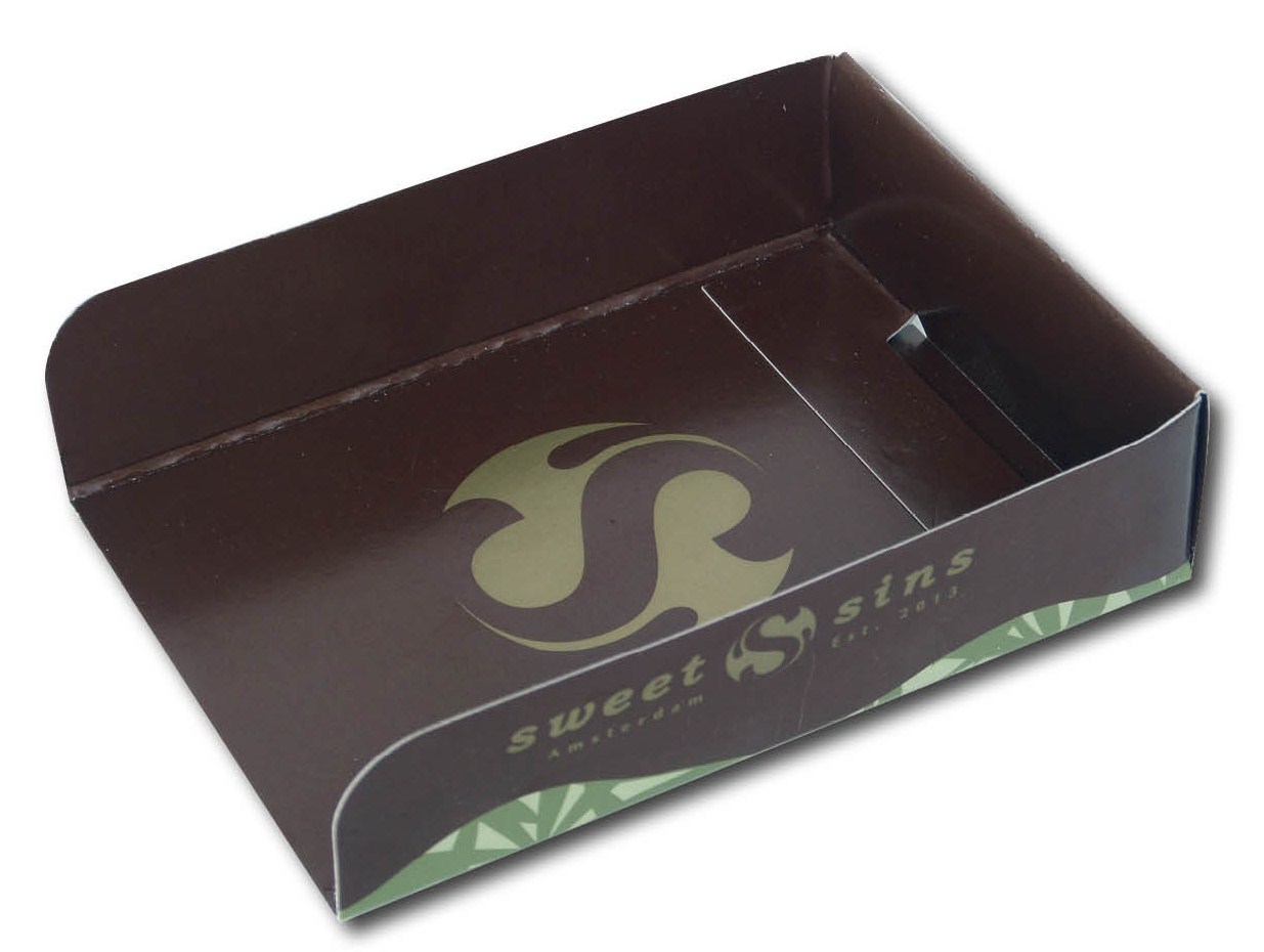 Bedrukte-doosjes.nl kartonnen tray op maat voor Sweet Sins Amsterdam met goudkleurig logo en de tekst Est. 2013 op een glanzende, donkerbruine achtergrond. Deze luxe kartonverpakking is uitgevoerd als een open presentatiebakje met een elegant, schuin aflopende voorrand en een subtiel groen grafisch patroon langs de onderzijde. De vrijstaande kartonnen bakjes worden rechtstreeks geproduceerd in de eigen drukkerij in Berkel en Rodenrijs zonder tussenpersonen. Beschikbaar in diverse standaardmaten om stanskosten te besparen en leverbaar in flexibele oplages van 50 tot 10.000+ stuks met een snelle logistieke afhandeling binnen de Benelux.