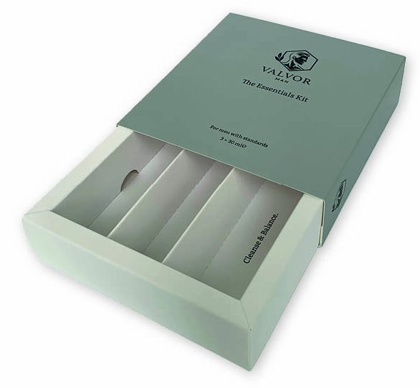 Luxe bedrukte grijze schuifdoos verpakking voor de 'Valvor Man Essentials Kit', met een witte uitschuiflade en op maat gemaakte inleg voor drie producten. De inleg is bedrukt met de namen van de producten.