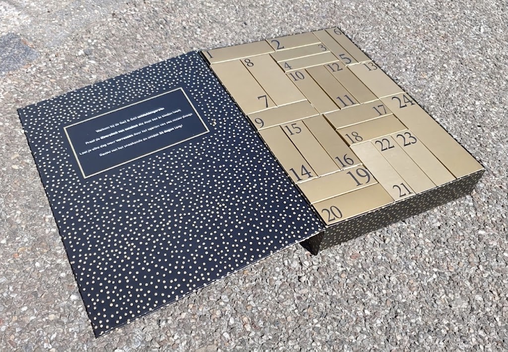 Luxe geopende bedrukte adventsdoos van karton op maat. Binnenkant voorzien van 24 losse gouden doosjes met nummering van 1 tot en met 24 en een bedrukte binnenzijde van de klep met een feestelijk gouden stip patroon.